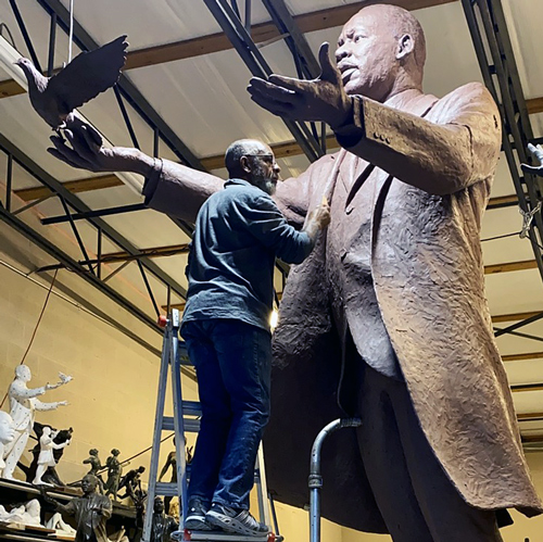 man standing on a ladder works on a large sculpture of martin luther king jr.