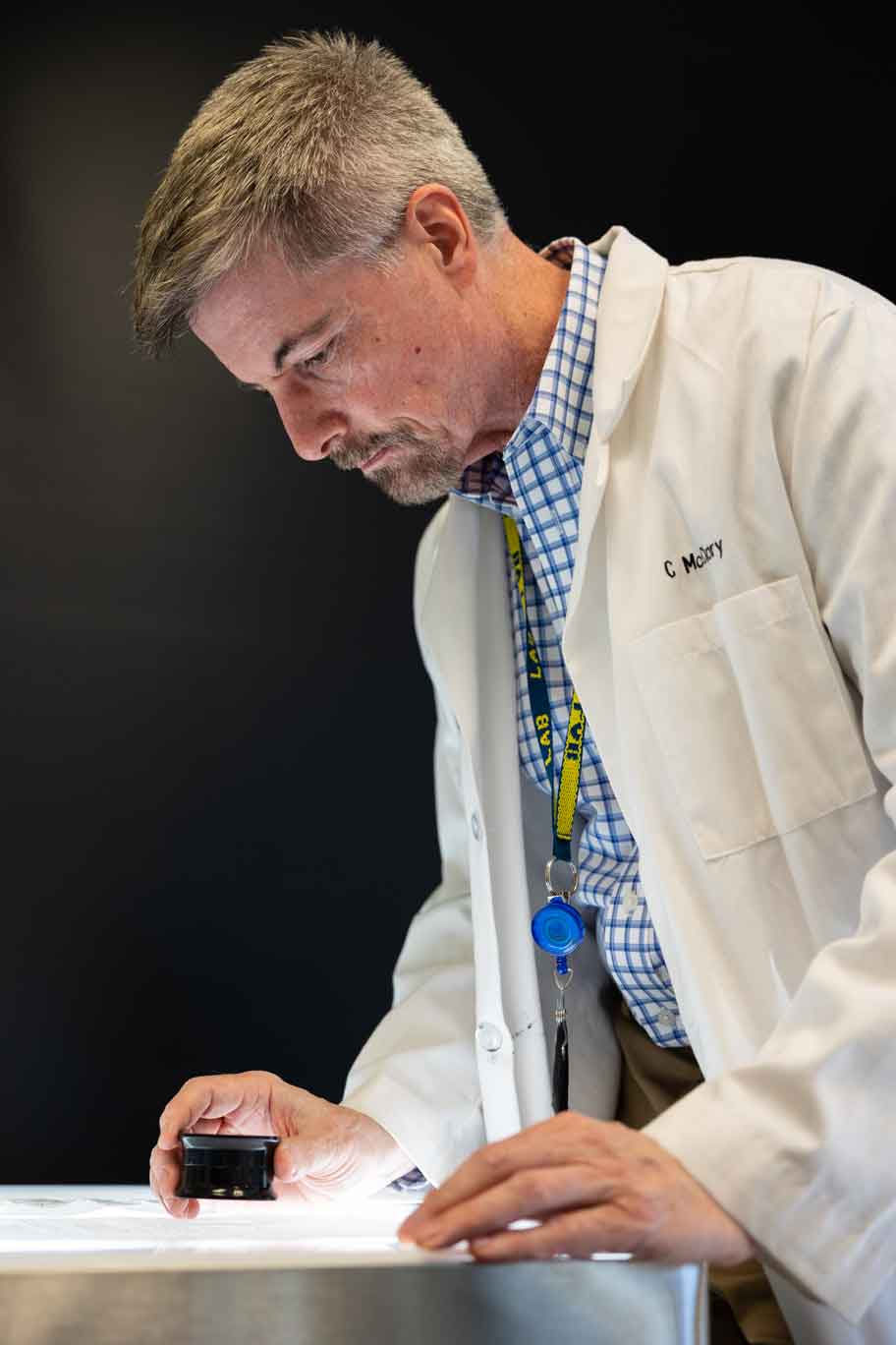 A scientist in a white lab coat studies evidence with a microscope