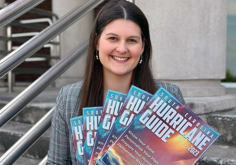Leah Blackwood stands on a staircase holding magazines with the title hurricane guide