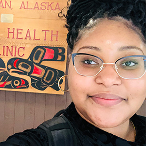 Chloe Watts stands in front of a sign for the health clinic in Alaska.
