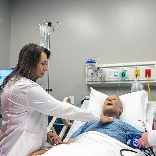 a woman in a white coat demonstrates a technique on a animatronic patient