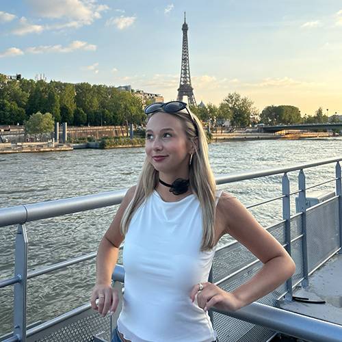 Priya Frazier enjoys a river cruise on the Seine, standing in front of the lit Eiffel Tower.