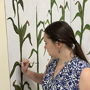 Center Visitor Coordinator Katelyn Shull paints a corn stalk during the exhibit's installation.