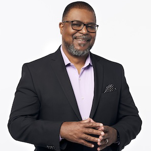 man wearing glasses smiles while wearing pink shirt and black blazer