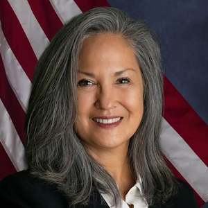 woman with gray hair smiling in front of american flag