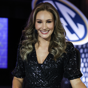 woman wearing microphone smiles in front of sign that reads SEC