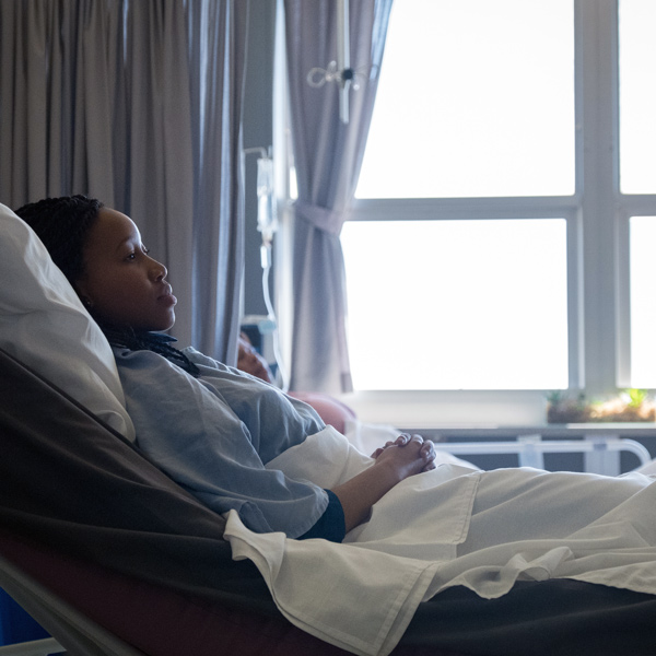 a woman lies in a hospital bed with a window in the background