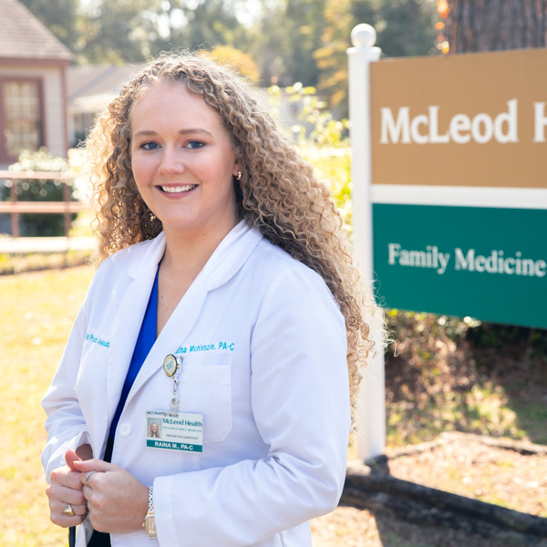 woman in a white coat stands in front of a sign with the words McLeod Family Medicine on it