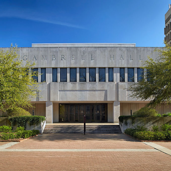 gray building with trees and a brick walkway in the foreground