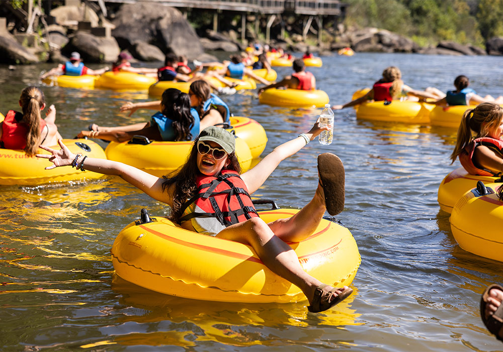 female student floating in yellow tube on the river with other students in background