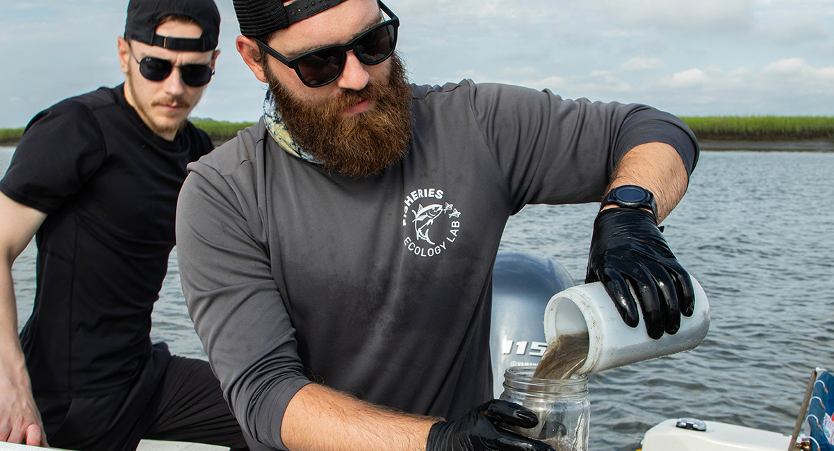 Two researchers in coastal estuary take water samples.