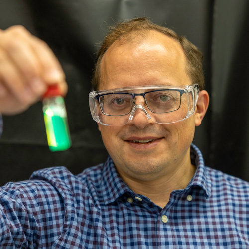 A man wearing protective glasses holds up a tube of fluorescent nanocrystals in a tube.