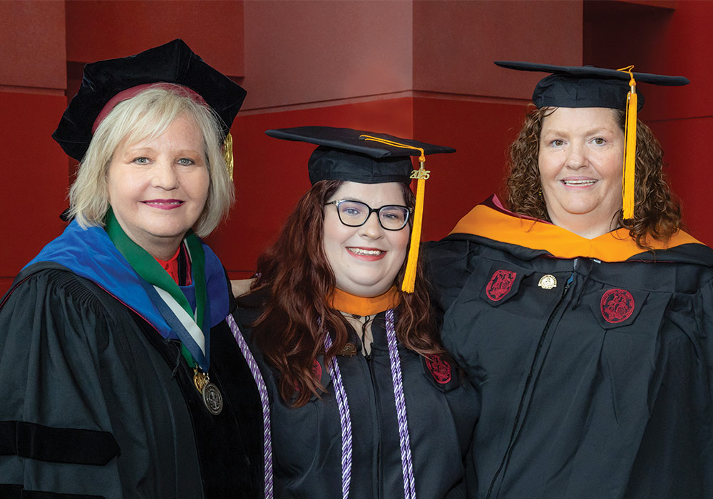three women in caps and gowns at nursing commencement