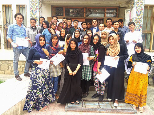 Young adults pose for a picture in front of an Afghan school. The students hold certificates.
