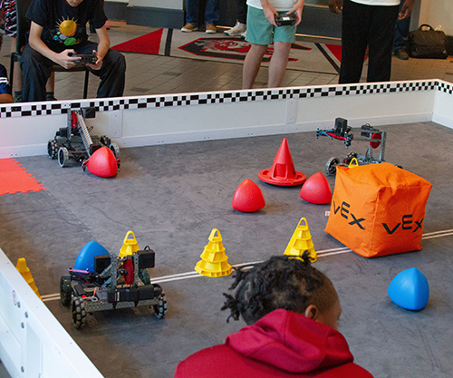 Students use remotes to control robots picking up small items.